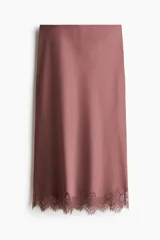 Pollera midi de tejido satinado color rosado con acabado brillante, corte recto y detalle de encaje festoneado en el ruedo.
