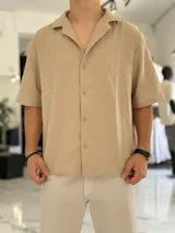 Camisa de lino color beige, de manga corta, con cuello abierto y cierre frontal de botones.