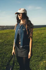 Chaleco de denim azul oscuro con costuras contrastantes en hilo ocre, cierre frontal con broches metálicos a presión y detalle de bordado ovalado en el pecho.