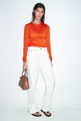 Bolso tipo mini shopper de cuero sintético color marrón caramelo, con costuras blancas visibles. Posee asas de mano y una correa bandolera ancha de tela color beige. El frente tiene un detalle de tira con hebilla metálica dorada.