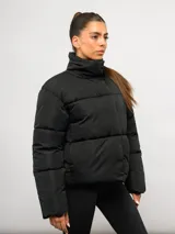 Campera puffer corta Umbro de color negro, con cuello alto, cierre frontal y bolsillos laterales. Presenta un diseño acolchado y logo de la marca bordado en el pecho.