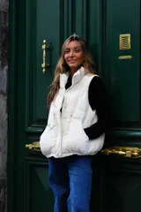 Chaleco puffer beige sin mangas, con cuello alto, cierre frontal con cremallera y bolsillos laterales.