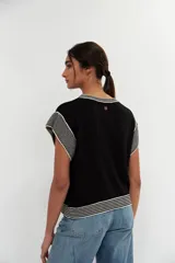 Top de tejido de punto en color negro, con cuello redondo, mangas cortas y detalles de rayas horizontales en blanco y negro en el cuello, las mangas y el ruedo.