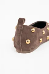 Chatita de gamuza color marrón con detalle de tachas metálicas doradas distribuidas por toda la superficie. Presenta una tira pequeña en el talón y diseño de punta redondeada.