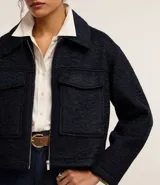 Campera corta azul marino de tejido boucle con cuello inglés, cierre frontal con cremallera y bolsillos grandes con solapa en el pecho.