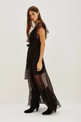 Vestido largo de gasa negra con estampado de puntos dorados, diseño cruzado con volados en el escote y falda, y forro interior corto.