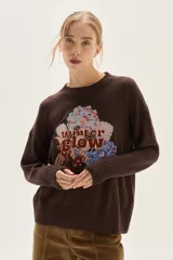 Sweater de tejido de punto color marrón oscuro, con cuello redondo y bordado frontal que incluye texto "Winter Glow" rodeado de motivos florales en tonos azules, rojos y blancos.