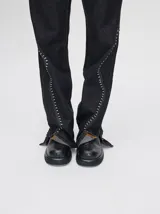 Pantalón de denim tiro alto con corte oxford y aberturas laterales en el bajo. Presenta apliques metalizados decorativos en los bolsillos delanteros y a lo largo de las costuras laterales.