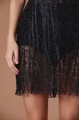 Vestido corto de fiesta color negro, con escote en V, confeccionado en tela con lentejuelas brillantes y transparencias. Presenta un diseño ajustado con falda de corte recto.