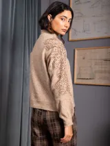 Buzo de cuello alto color gris, de manga larga, con detalle de bordado floral con lentejuelas en el hombro y parte superior de la manga.