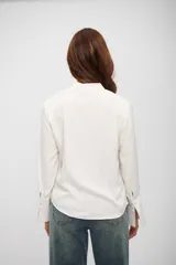 Blusa de color blanco con cuello en V y mangas largas con puños acampanados y detalle de frunces.