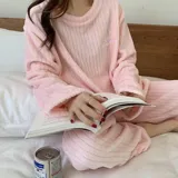 Conjunto de pijama de dos piezas confeccionado en tela de plush texturizada con diseño de rayas verticales en relieve. Incluye una remera de manga larga con cuello redondo y un pantalón de corte holgado. La remera presenta un pequeño bordado decorativo en el pecho.