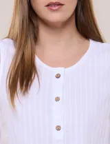 Blusa blanca sin mangas, confeccionada en algodón con sutiles rayas verticales en relieve. Presenta cuello redondo, cierre frontal con botones de madera y un nudo ajustable en el dobladillo delantero.