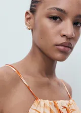 Vestido largo de corte recto y tejido fluido, con estampado de palmeras en tonos naranjas sobre fondo crema. Presenta cuello halter con detalle fruncido, tirantes finos ajustables y cierre de lazo en la espalda.