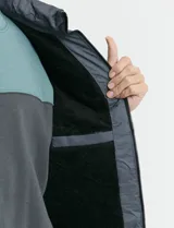Chaleco capitoneado de color azul marino, con capucha desmontable, cierre frontal y bolsillos laterales con detalles en naranja. Presenta un diseño acolchado con costuras horizontales.