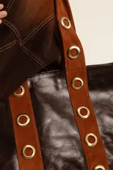 Cartera tipo tote de cuero color marrón, con detalles de cuero con pelo estampado animal print en las asas y ojales metálicos decorativos.