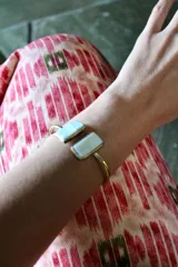 Pulsera rígida dorada con dos piedras rectangulares de color blanco nacarado en los extremos.