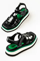 Sandalias negras con tiras anchas, plataforma blanca y detalles en verde.