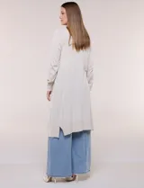Cardigan largo de punto liviano y suave, de color blanco, con diseño abierto al frente, mangas largas con puños acanalados y bolsillos frontales aplicados.