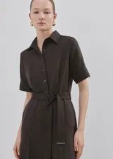 Mono largo de lino y lyocell en color marrón, con diseño recto, cuello camisero, manga corta, bolsillos laterales y cierre delantero con botones. Incluye un cinturón ajustable del mismo tejido con hebilla metálica.