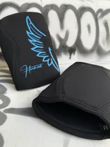 Par de rodilleras negras de neopreno de 7mm con logo de alas y nombre de la marca en color celeste.