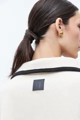 Capa color crudo con cuello camisero y ribetes negros. Cierre frontal con alamares negros y bolsillos laterales.