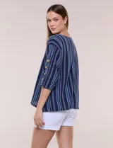 Blusa Erika de algodón con estampado de rayas en tonos azules, rosados y amarillos. Presenta cuello redondo con escote en V y botones frontales, mangas cortas decoradas con una fila de botones en los laterales y dobladillo asimétrico.