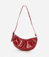 Cartera tipo shoulder bag de diseño media luna, confeccionada en poliuretano con acabado brillante. Presenta detalles frontales estilo gota, cierre superior por cremallera y correa de hombro ajustable con ojetes metálicos.