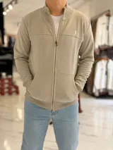 Campera de felpa color beige con cierre frontal, cuello alto y bolsillos tipo canguro.