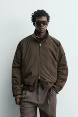 Cazadora bomber de corte relajado confeccionada en tejido técnico color negro. Presenta cuello subido, manga larga amplia, bolsillos de vivo en cadera, acabados elásticos y cierre frontal con cremallera de doble dirección.