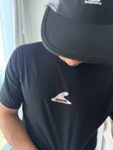 Remera negra de manga corta con estampado gráfico en la espalda que incluye un sol amarillo, una estrella de mar, una flor, una ola con el logo 'Brokers' y formas abstractas en tonos pastel, junto al texto 'VITAMIN SEA'.