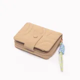 Billetera pequeña color beige con cierre de cremallera y detalle de cordón decorativo azul y amarillo.