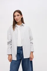 Camisa de corte oversize con diseño de rayas verticales finas en tonos claros. Presenta cuello clásico, cierre frontal con botones y mangas largas con puños abotonados.