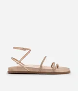 Sandalia plana marca Satinato, color oro rosado metalizado, con tiras finas decoradas con strass y cierre mediante hebilla en el tobillo.