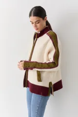 Campera de tejido de punto con cierre frontal, cuello alto y diseño color block en tonos marrón, rosa y rojo. Presenta detalles de trenzas en las mangas y puños y ruedo acanalados.