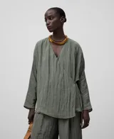 Blusa verde oliva de tejido arrugado con poliéster reciclado. Escote pico, manga japonesa, delantero cruzado y ata lateralmente con tira estrecha del mismo tejido.
