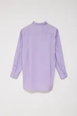 Camisa oversize color lavanda de poplin con cuello clásico, cierre frontal con botones, manga larga con puños abotonados y bolsillo de parche en el pecho.