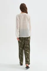 Blusa blanca de poliéster con cuello en V, volados frontales y mangas largas con elástico en los puños.