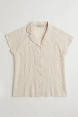 Camisa blanca de manga corta con cuello solapa, cierre frontal de botones y diseño bordado en hilo azul marino con motivos florales y vegetales.