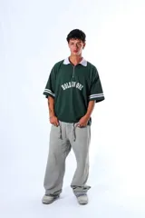 Chomba de piqué color verde con cuello polo blanco y cierre frontal parcial. Presenta un diseño holgado con mangas cortas que incluyen rayas blancas en los puños y un aplique frontal con el texto 'HOLE IN ONE' en color blanco.