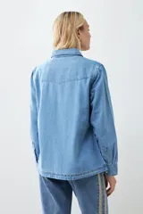 Camisa de jean celeste con cuello clásico, cierre frontal con botones a presión, dos bolsillos con solapa abotonada en el pecho y mangas largas con puños abotonados.