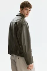 Cazadora estilo bomber en tejido revestido color verde militar, con cuello clásico, cierre frontal de cremallera metálica, bolsillos laterales y elástico fruncido en el bajo y los puños.