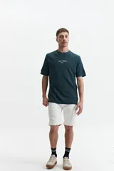 Remera de manga corta, color verde oscuro, con textura tipo waffle o piqué. Presenta un estampado vertical en la espalda con texto en blanco.