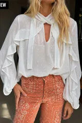 Blusa blanca de gasa con detalles estampados dorados, mangas largas abullonadas con volados, escote en V con lazo para anudar al cuello y diseño liviano con leve transparencia.