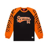 Camiseta de manga larga con diseño raglán, cuerpo negro y mangas naranjas con estampado de rayas de tigre. Presenta el logo de Supreme y el número 94 en el frente.