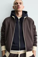 Sudadera de corte relajado en color azul marino con cuello alto y cierre frontal de cremallera. Presenta bandas laterales en color crema a contraste que recorren las mangas, puños y bajo en tejido rib, y bolsillos laterales de vivo.