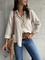 Camisa de color beige con cuello clásico, cierre frontal de botones y mangas largas con puños doblados. Presenta un delicado bordado floral en las mangas.