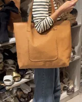 Bolso tote de cuero color marrón claro, con costuras decorativas verticales en los laterales y asa doble de hombro.