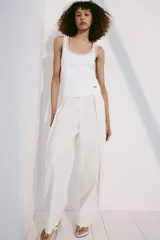 Musculosa de algodón color blanco con cuello redondo amplio y sisas. Cuenta con detalles de ribetes dorados brillantes en el escote, tirantes y costuras laterales.