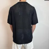 Camisa de tejido de punto calado en color beige, con cuello polo, cierre frontal de botones y mangas cortas.
